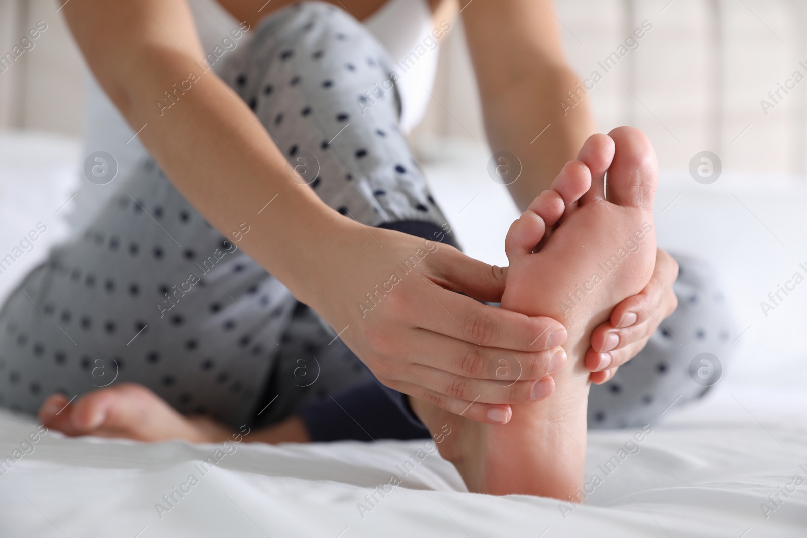 Photo of Young woman suffering from pain in foot on bed, closeup