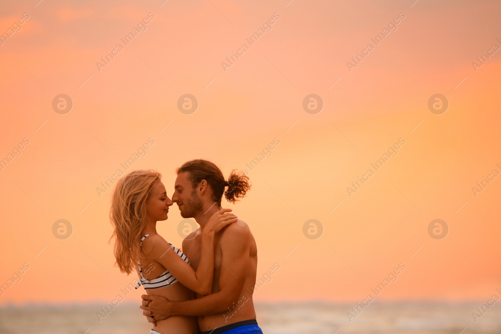 Photo of Young woman in bikini and her boyfriend on beach at sunset. Lovely couple