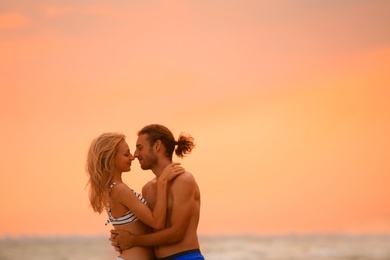 Young woman in bikini and her boyfriend on beach at sunset. Lovely couple