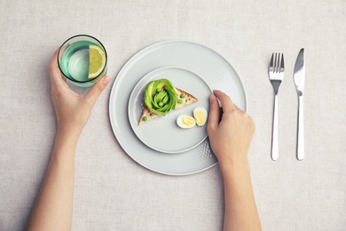 Woman eating crisp toast with avocado and quail egg on table, top view