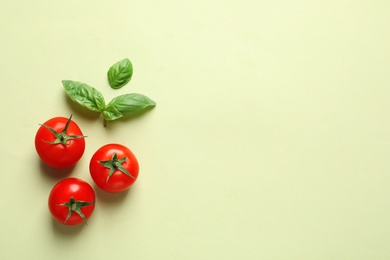 Flat lay composition with ripe cherry tomatoes and basil leaves on color background. Space for text