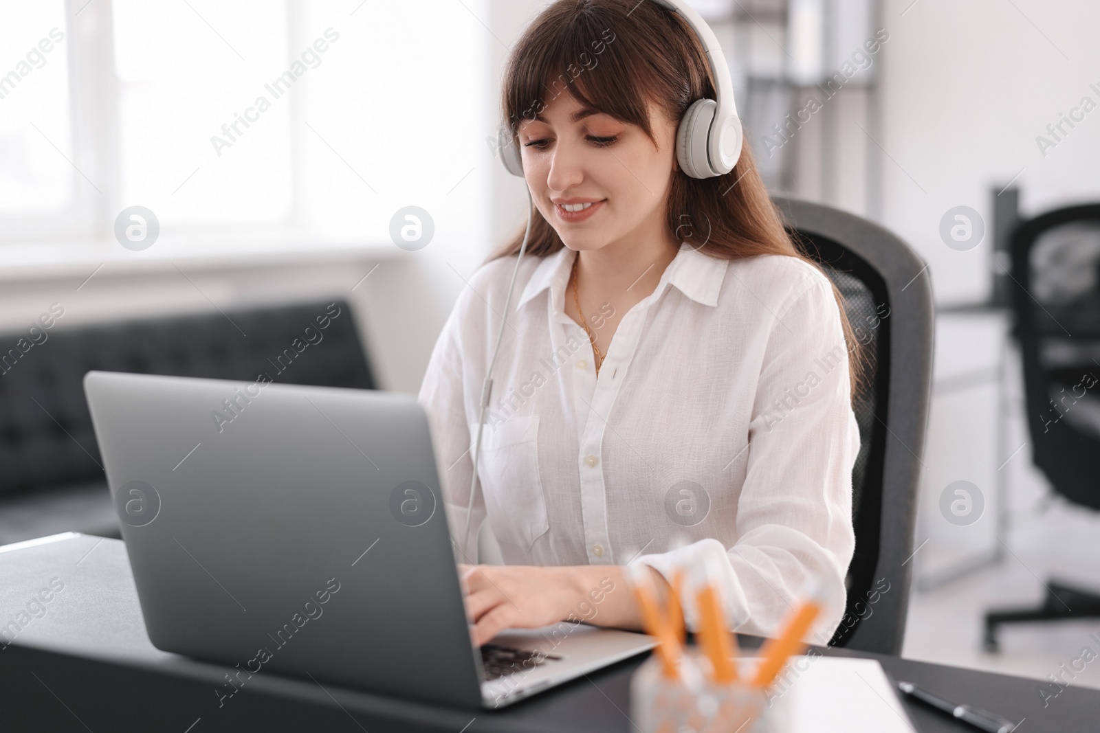 Photo of Woman in headphones watching webinar at table in office