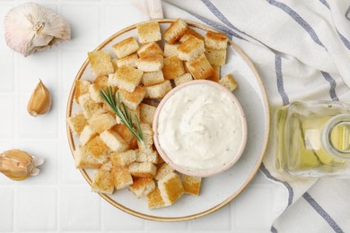 Photo of Delicious crispy croutons with rosemary and sauce on white tiled table, flat lay