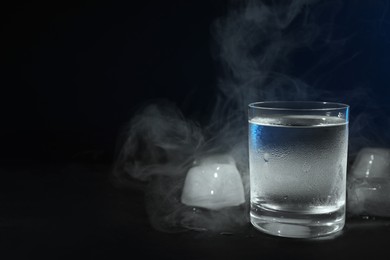 Photo of Vodka in shot glass with ice on black table against dark background