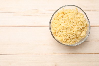 Photo of Delicious bulgur in glass bowl on wooden table, top view. Space for text