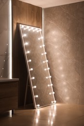 Modern mirror with light bulbs near wooden wall in room