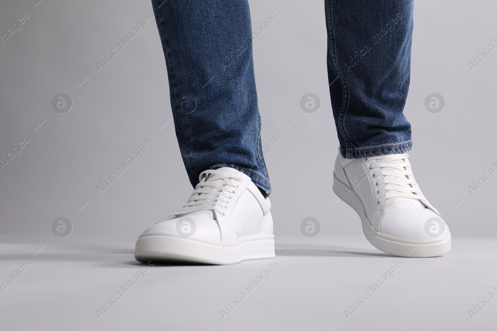 Photo of Man wearing stylish white sneakers on grey background, closeup