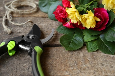 Photo of Secateur, beautiful roses and rope on wooden table, closeup