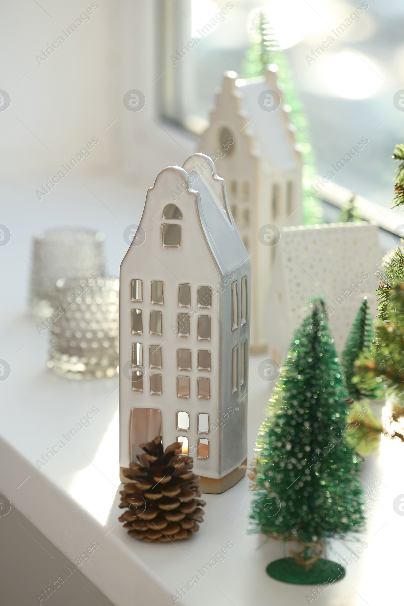 Photo of Beautiful house shaped candle holders and small fir trees on windowsill indoors