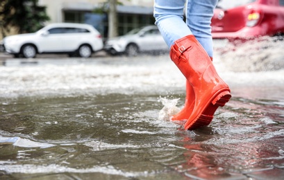 Woman with rubber boots running in puddle, closeup. Rainy weather