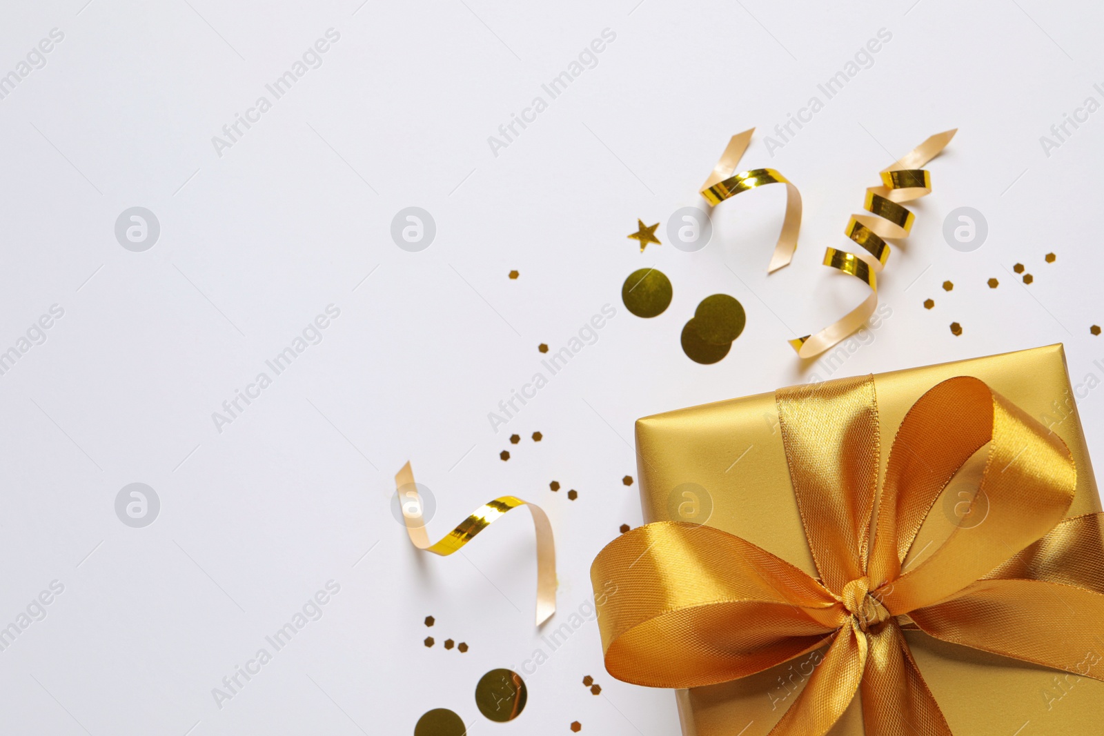 Photo of Beautiful golden gift box and confetti on white background, flat lay. Space for text