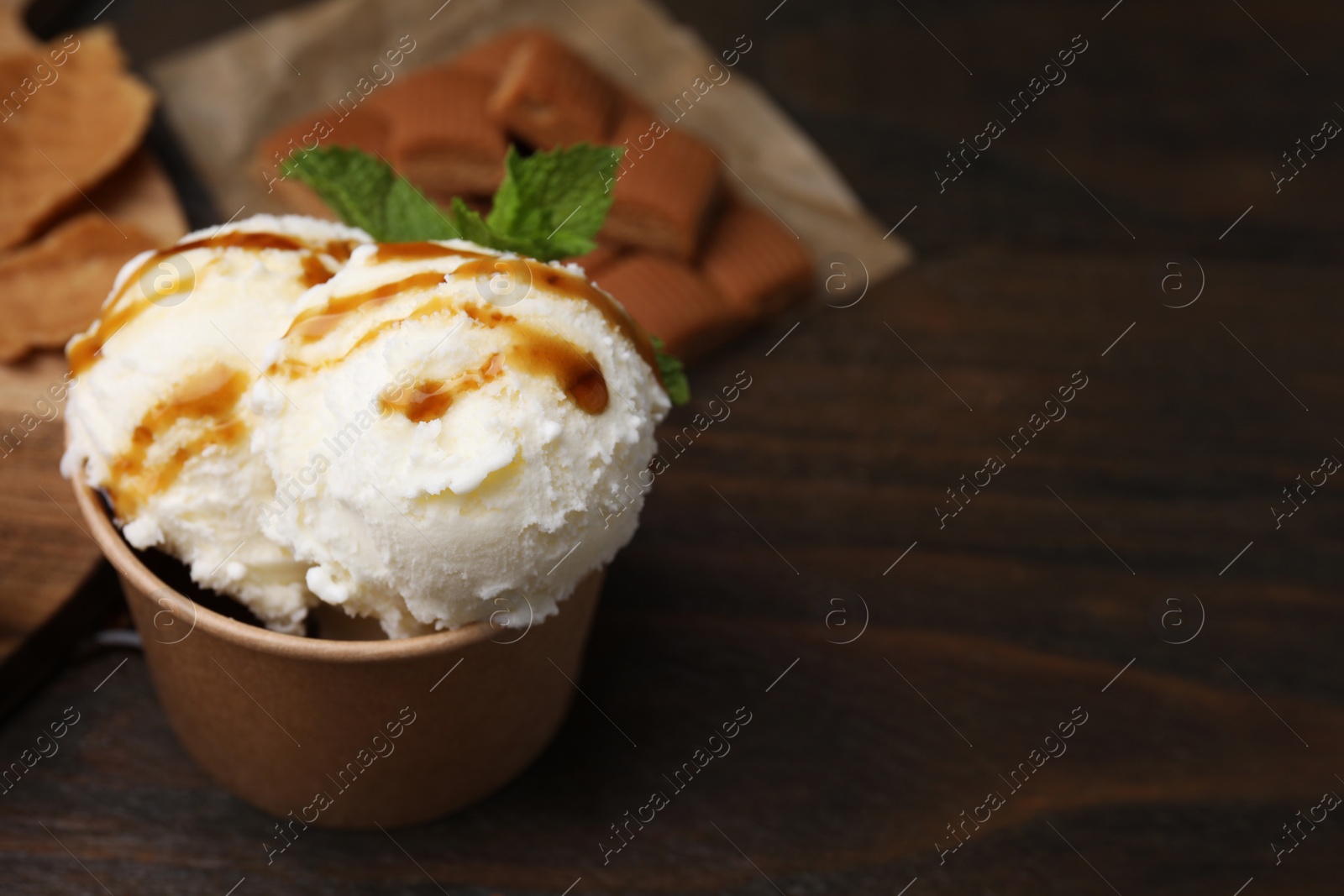 Photo of Scoops of tasty ice cream with caramel sauce and mint on wooden table, closeup. Space for text