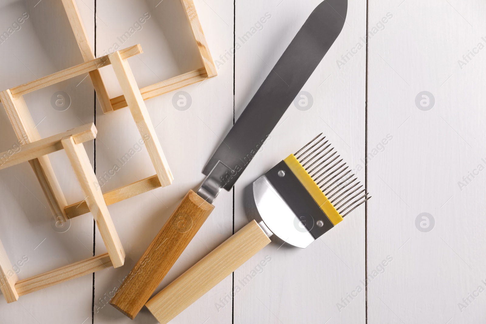 Photo of Honeycomb frames and beekeeping tools on white wooden table, flat lay