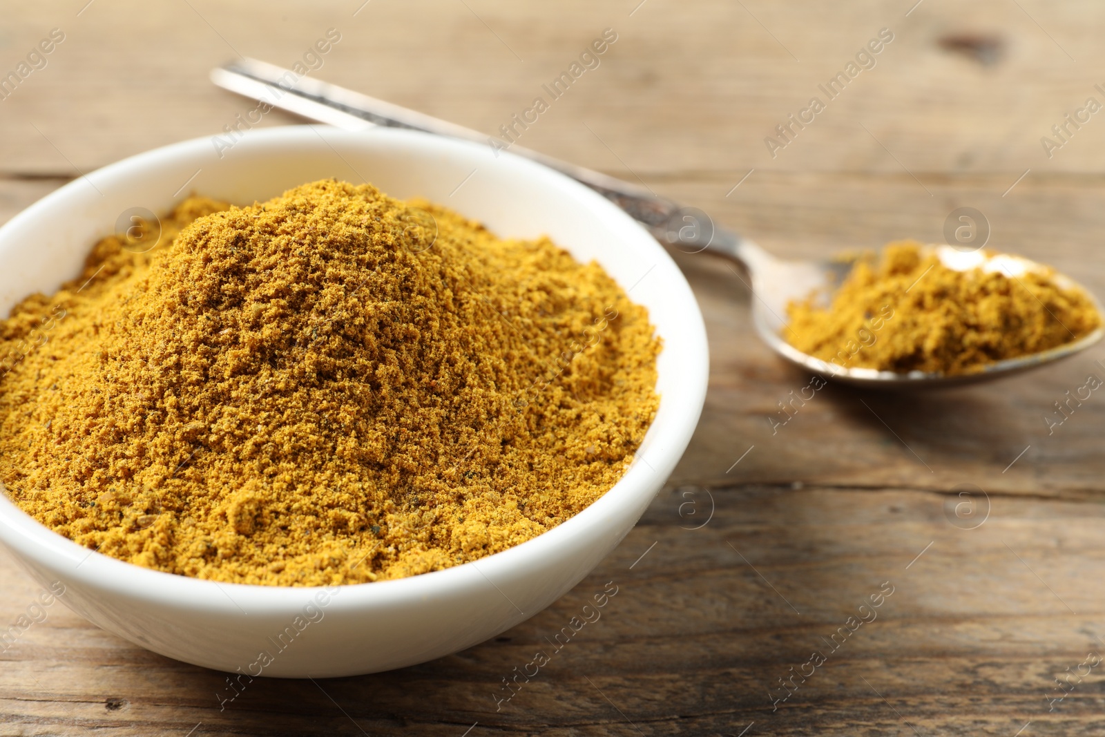 Photo of Dry curry powder in bowl and spoon on wooden table, closeup