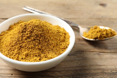 Photo of Dry curry powder in bowl and spoon on wooden table, closeup