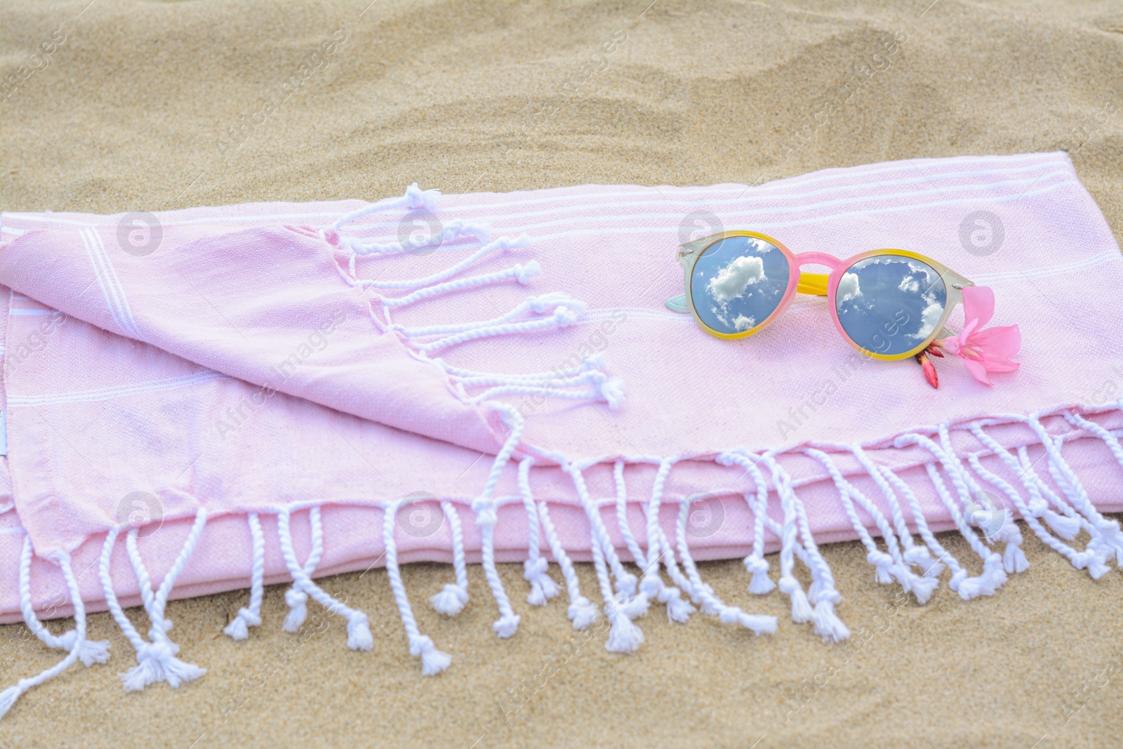 Photo of Blanket with stylish sunglasses and flower on sand outdoors. Beach accessories