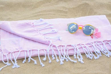 Blanket with stylish sunglasses and flower on sand outdoors. Beach accessories