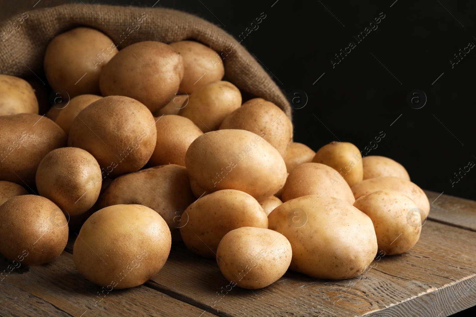 Photo of Raw fresh organic potatoes on wooden table against dark background