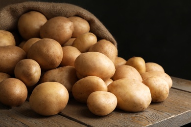 Photo of Raw fresh organic potatoes on wooden table against dark background