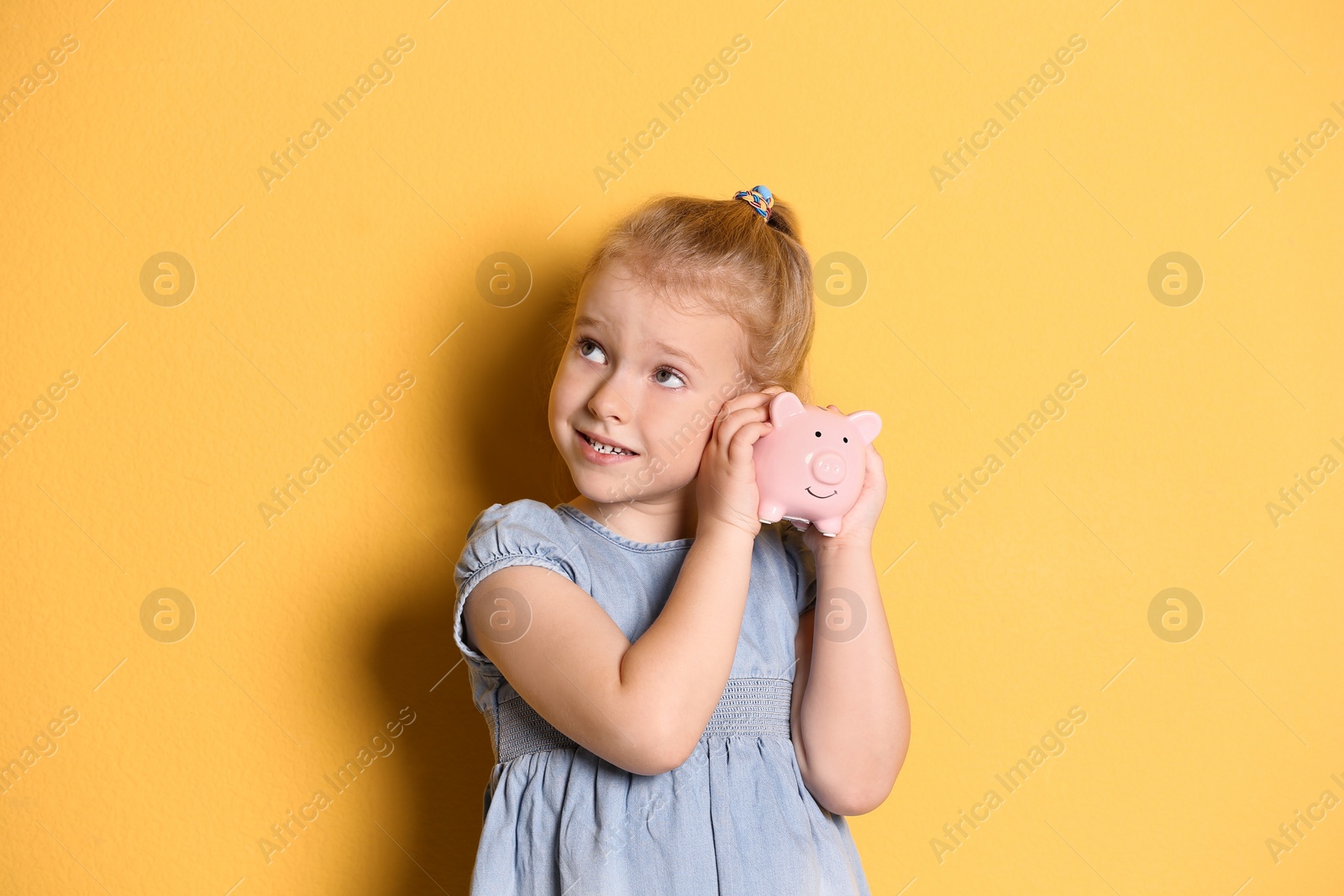 Photo of Little girl with piggy bank on color background