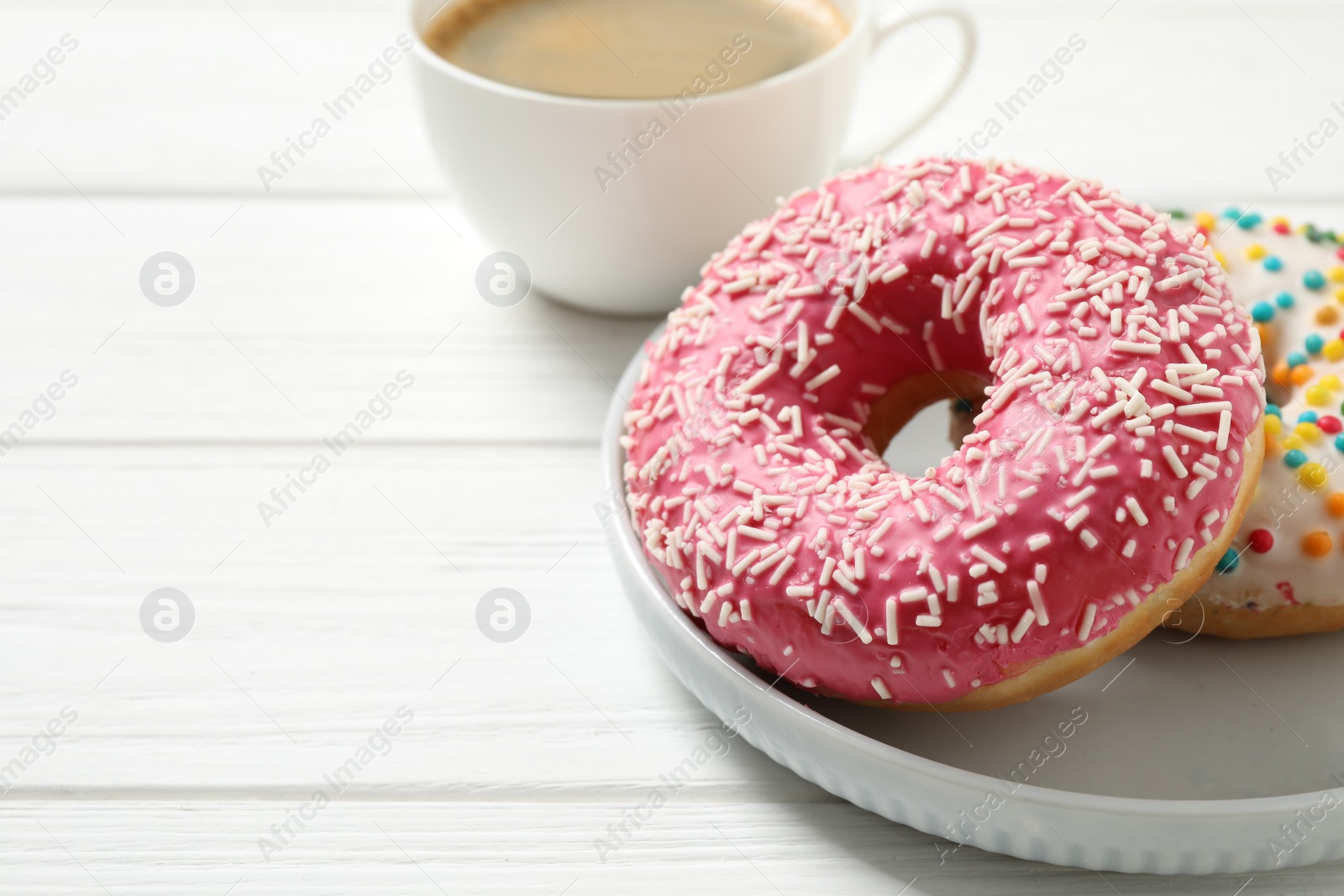 Photo of Yummy donuts with sprinkles on white wooden table, closeup. Space for text