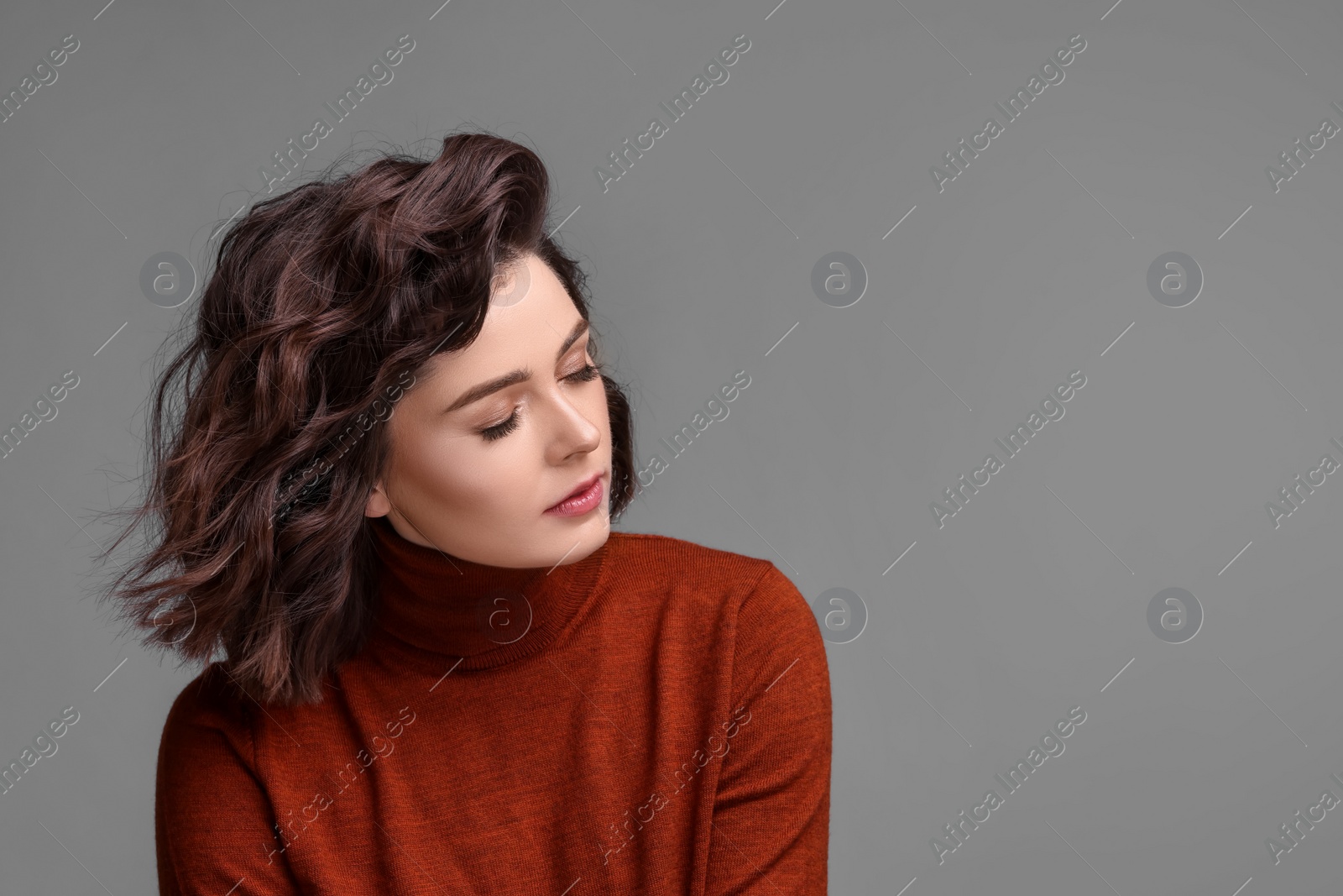 Photo of Portrait of beautiful young woman with wavy hairstyle on grey background. Space for text