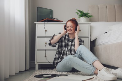 Photo of Young woman listening to music with turntable in bedroom