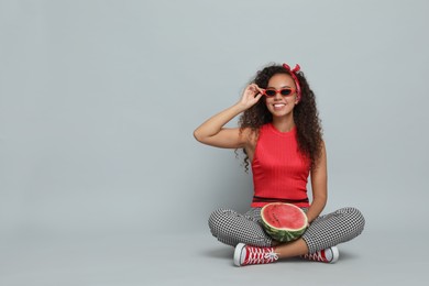 Photo of Beautiful young African American woman with half of watermelon on grey background. Space for text