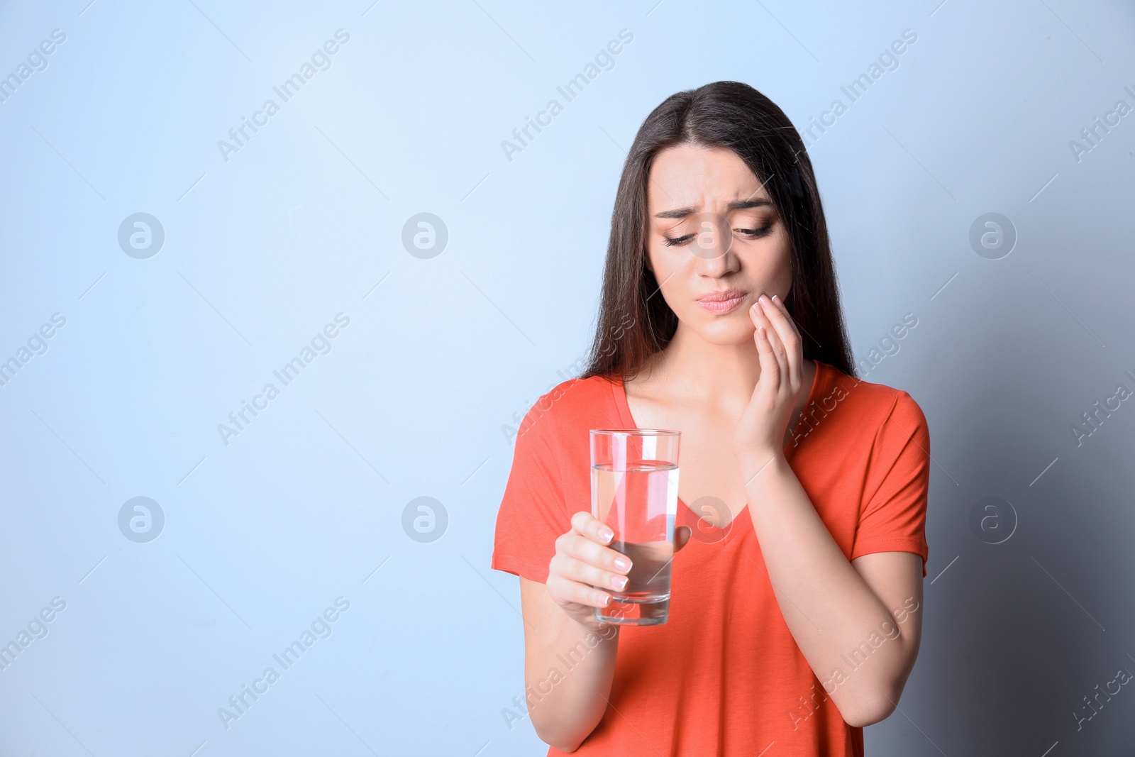 Photo of Woman with sensitive teeth holding glass of water on color background