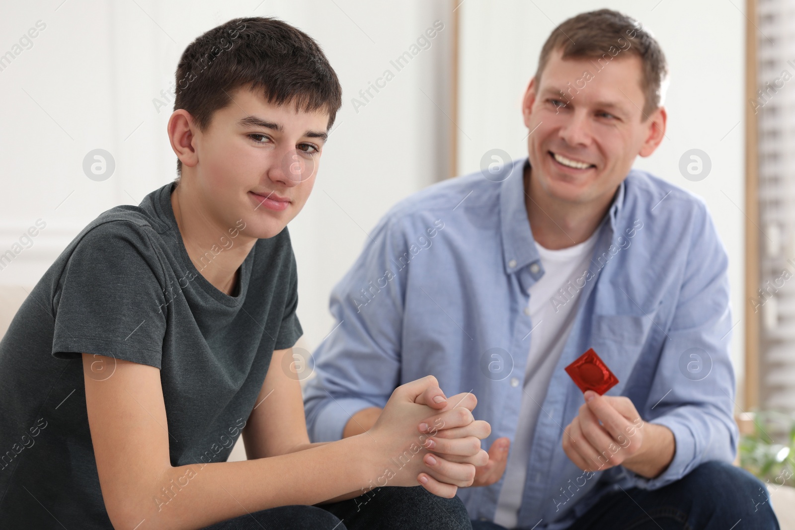 Photo of Father talking with his teenage son about contraception at home. Sex education concept