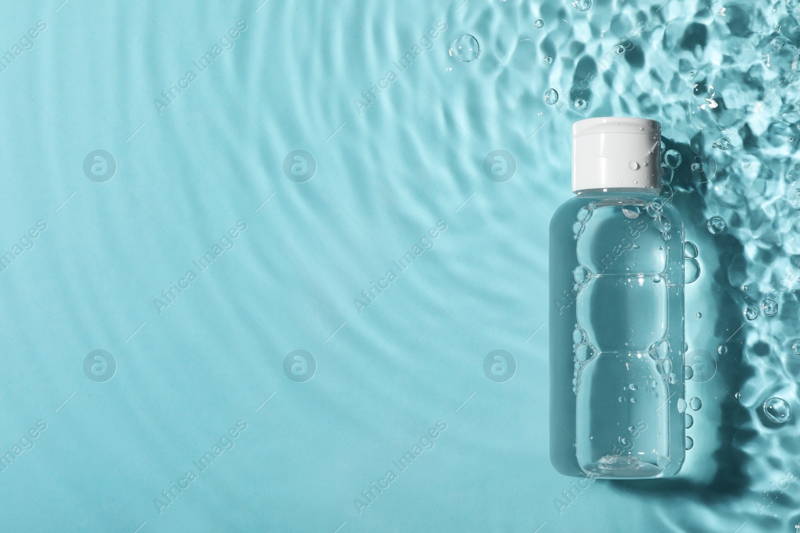 Photo of Wet bottle of micellar water on light blue background, top view. Space for text