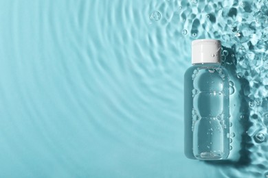 Photo of Wet bottle of micellar water on light blue background, top view. Space for text
