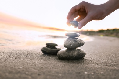 Photo of Woman stacking dark stones on sand near sea, space for text. Zen concept