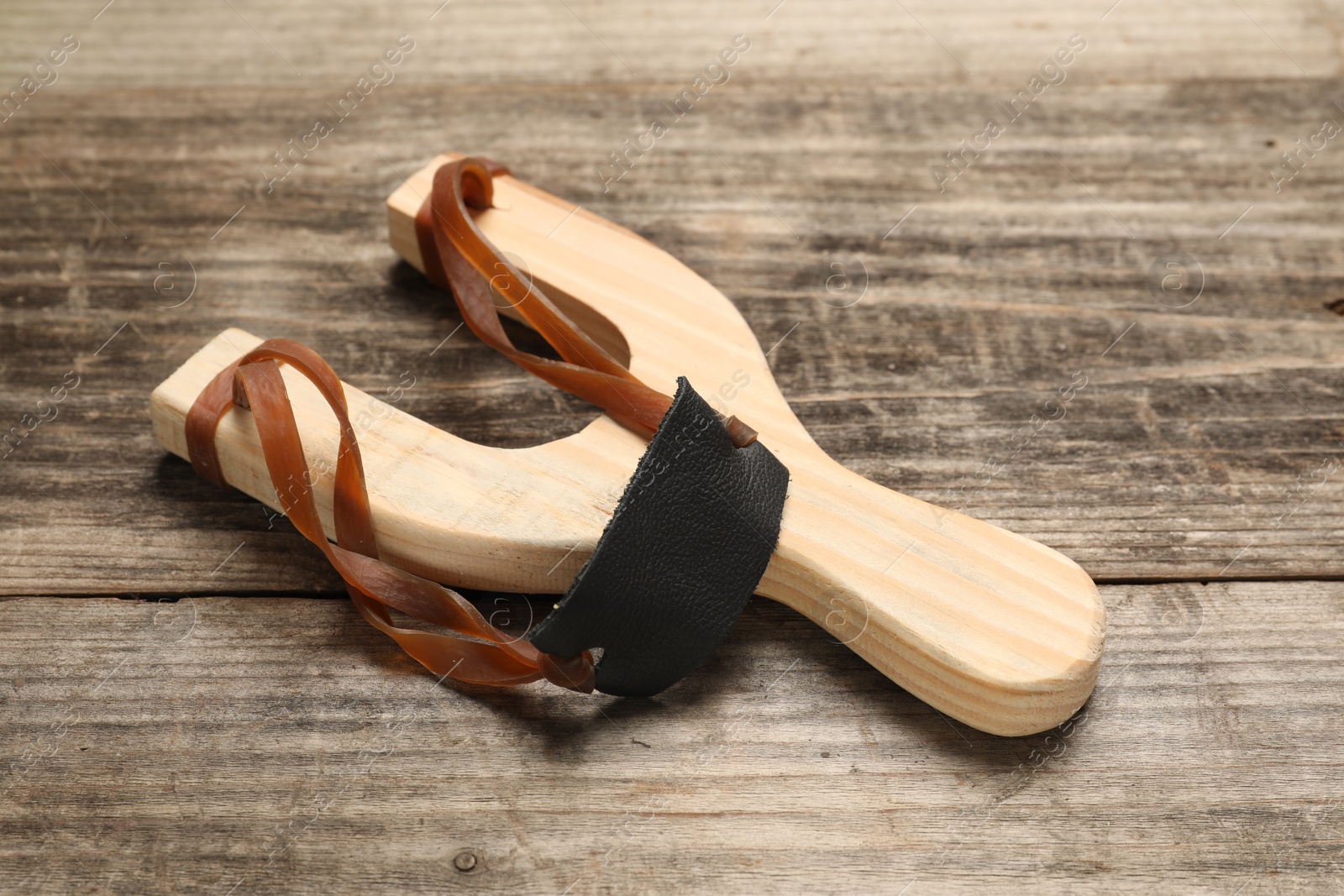 Photo of Slingshot with leather pouch on wooden table, closeup