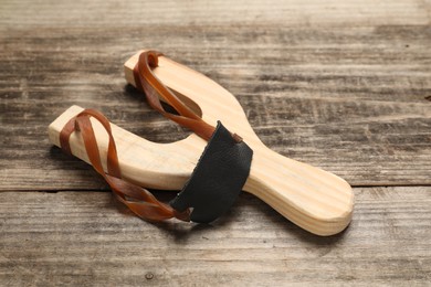 Photo of Slingshot with leather pouch on wooden table, closeup