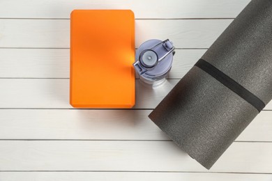 Exercise mat, yoga block and bottle of water on white wooden floor, flat lay