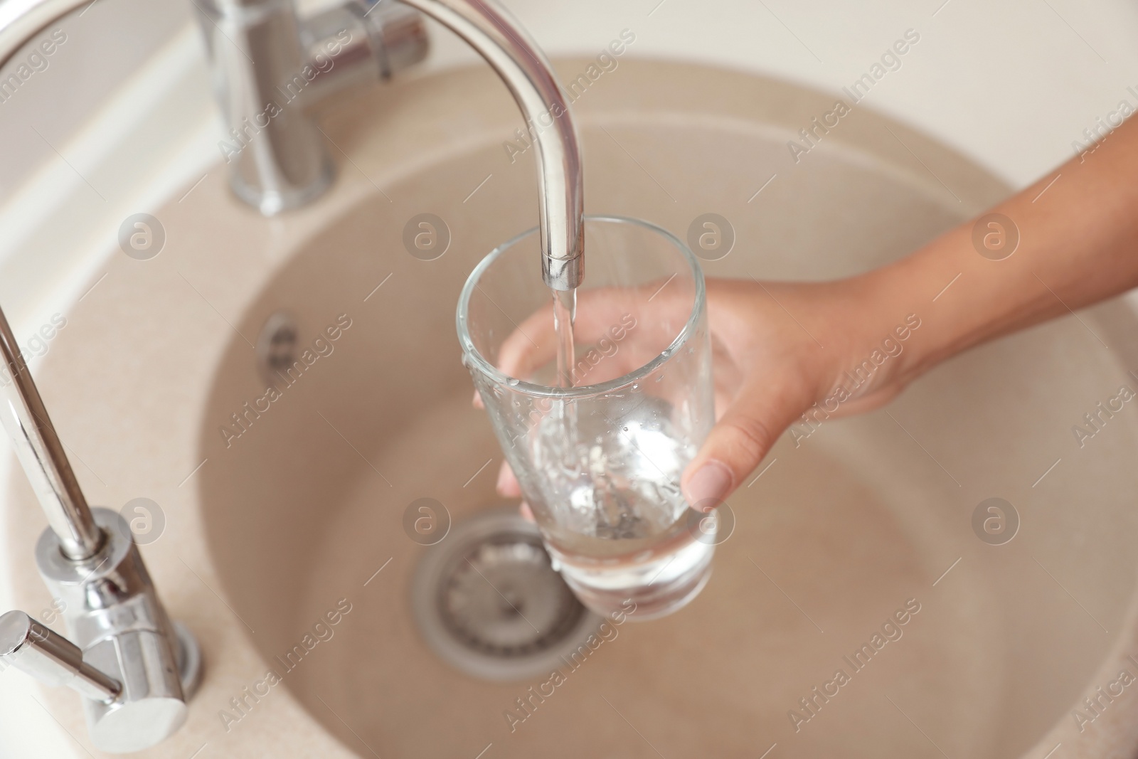 Photo of Woman pouring water into glass in kitchen, closeup