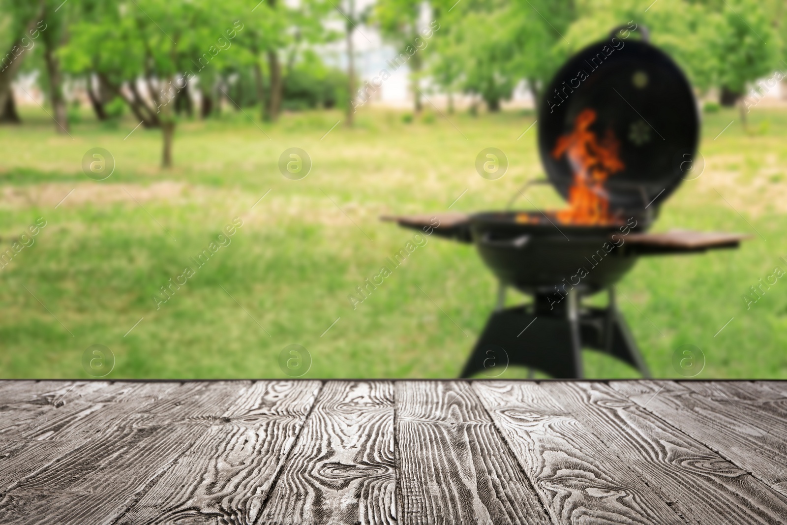 Image of Empty wooden table and blurred view of modern barbecue grill with fire flames outdoors