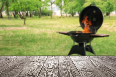 Image of Empty wooden table and blurred view of modern barbecue grill with fire flames outdoors