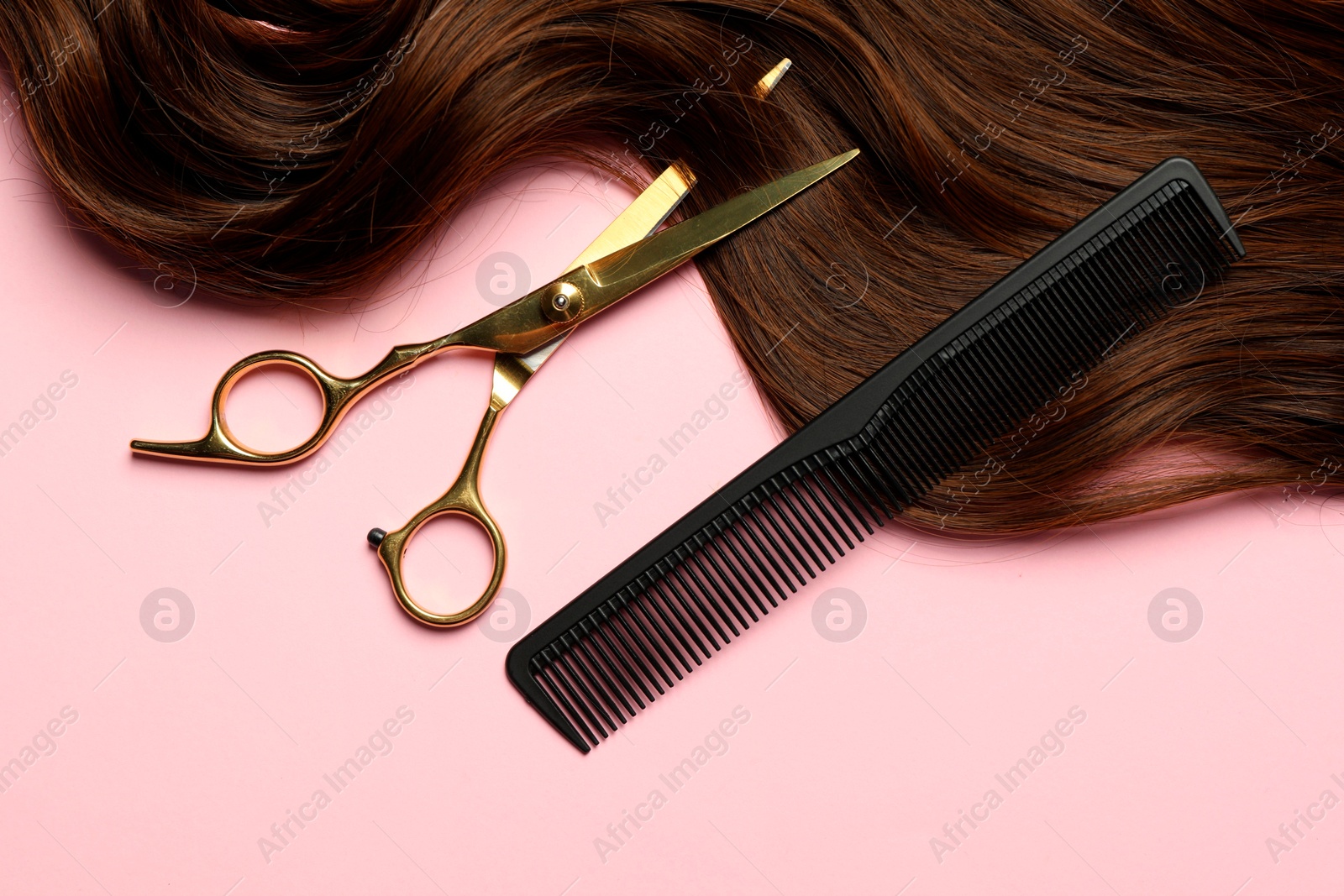 Photo of Professional hairdresser scissors and comb with brown hair strand on pink background, flat lay
