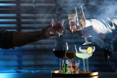 Photo of People with different alcohol drinks clinking glasses indoors, closeup
