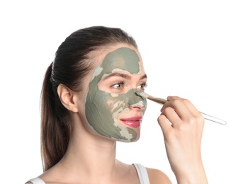 Photo of Young woman applying clay mask on her face against white background. Skin care