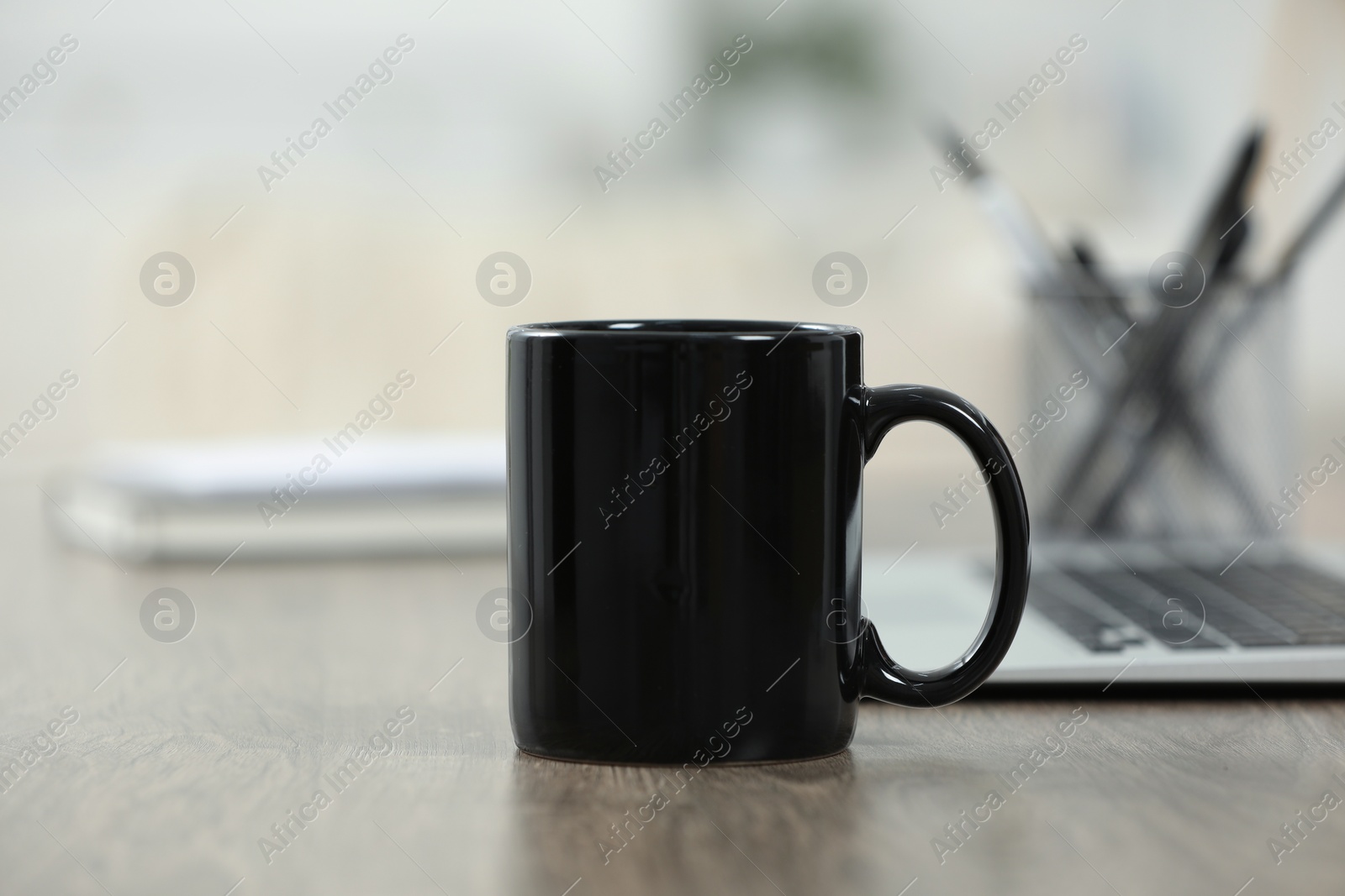 Photo of Black ceramic mug and laptop on wooden table indoors. Space for text