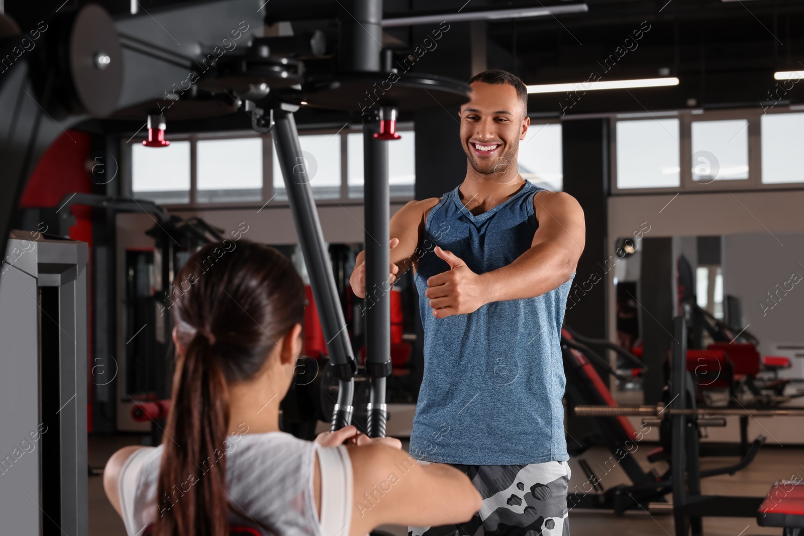 Photo of Happy trainer explaining woman how to do exercise properly in modern gym