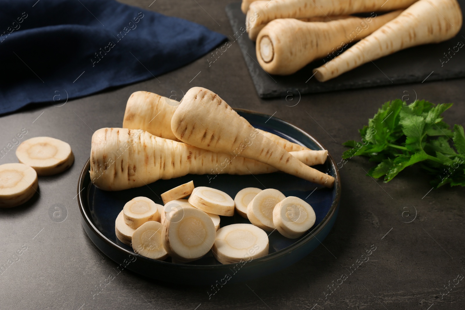Photo of Whole and cut parsnips on black table