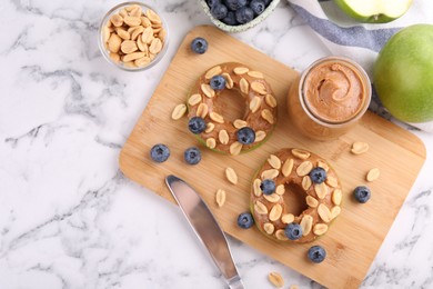 Photo of Fresh green apples with peanut butter, blueberries and nuts on white marble table, flat lay. Space for text
