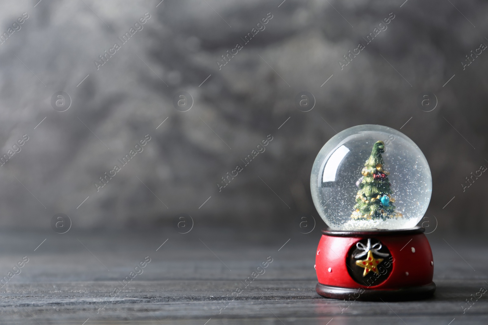 Photo of Snow globe with Christmas tree on grey wooden table, space for text