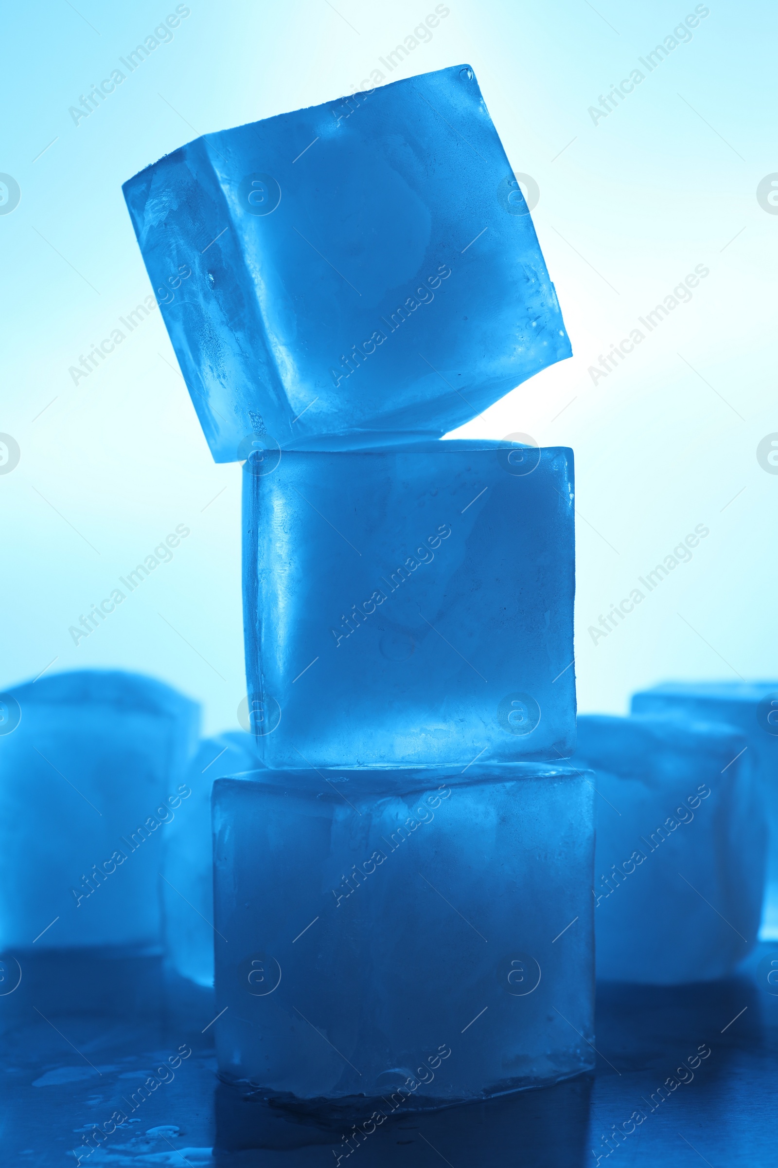 Photo of Stack of crystal clear ice cubes on light blue background. Color tone effect