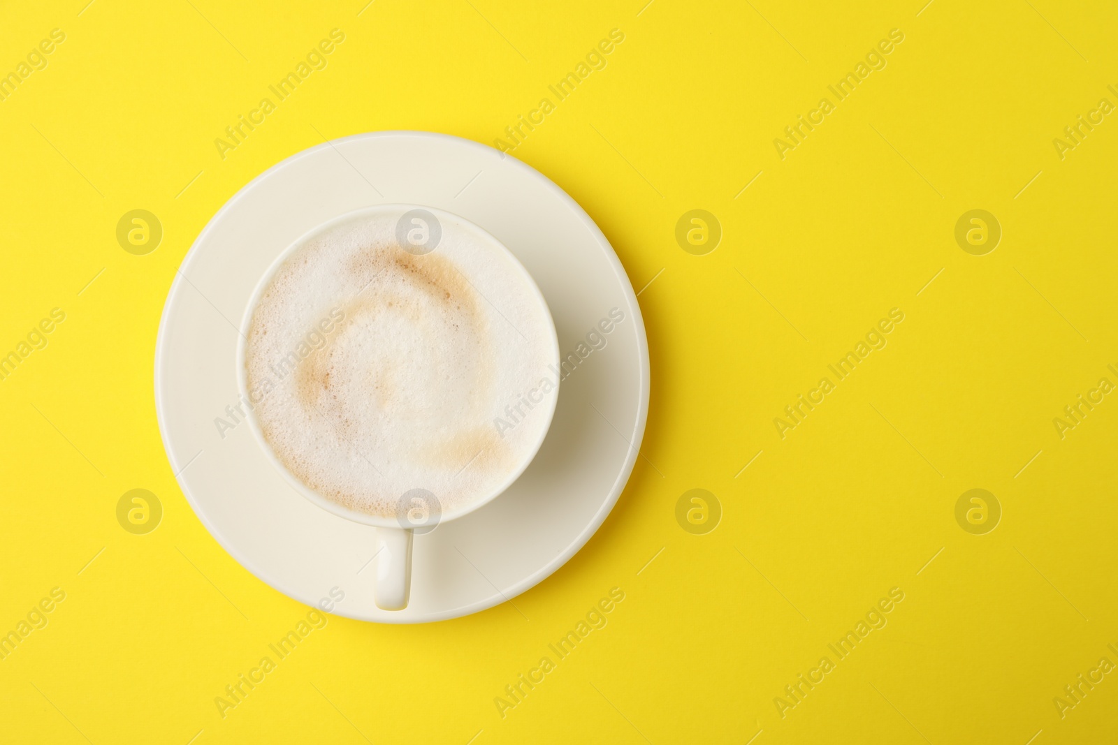 Photo of Tasty cappuccino in coffee cup on yellow background, top view. Space for text