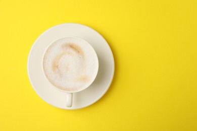 Photo of Tasty cappuccino in coffee cup on yellow background, top view. Space for text